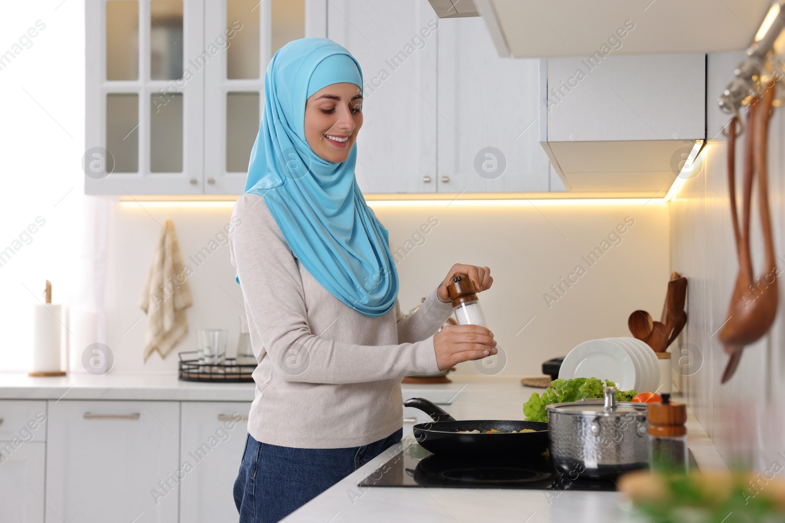 Photo of Muslim woman cooking dish in frying pan on cooktop indoors