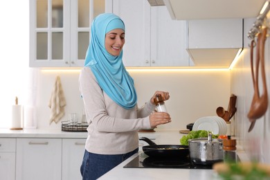 Muslim woman cooking dish in frying pan on cooktop indoors