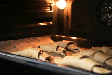 Photo of Baking sheet with raw croissants in oven, closeup