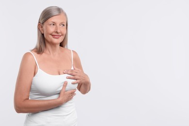 Photo of Beautiful senior woman doing breast self-examination on white background, space for text