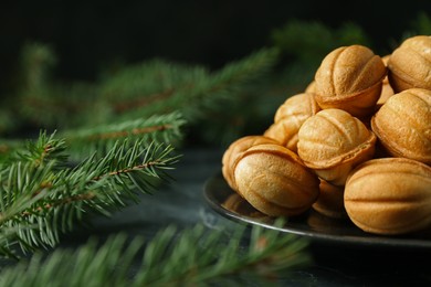 Plate of tasty nut shaped cookies near fir branches on black table, closeup