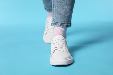 Photo of Woman wearing stylish white sneakers on light blue background, closeup