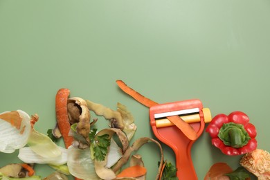 Photo of Peels of fresh vegetables and peeler on green background, flat lay. Space for text