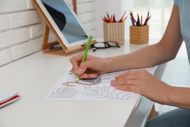 Photo of Young woman coloring antistress page at desk indoors, closeup