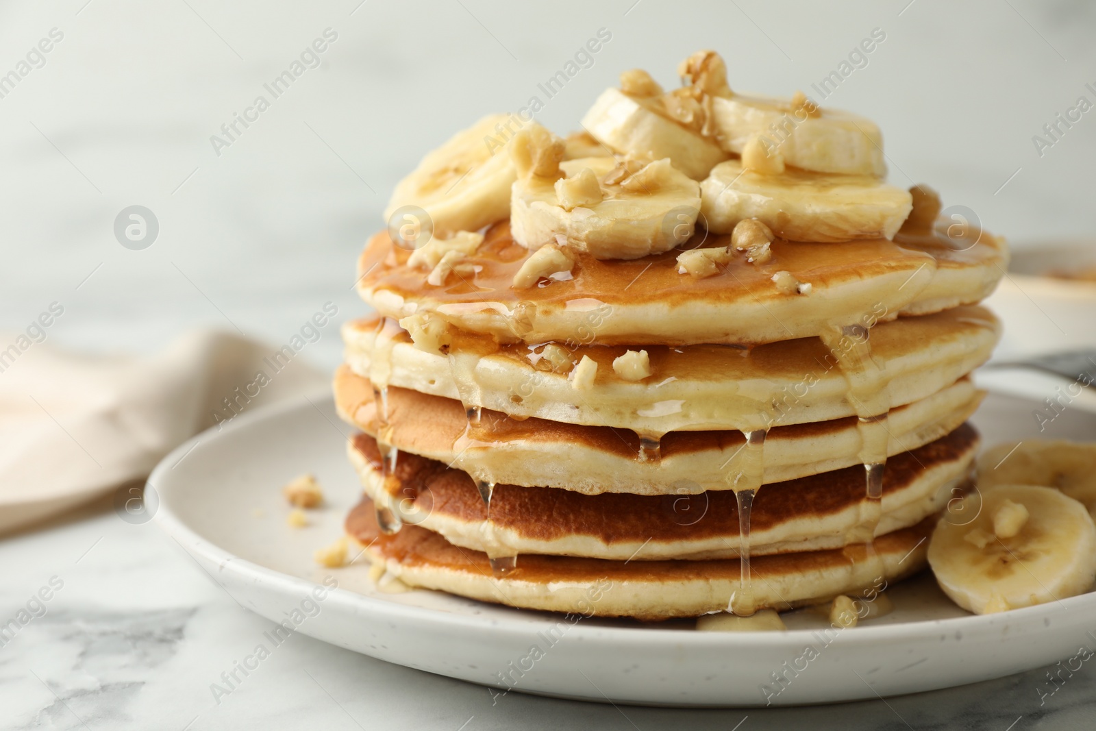 Photo of Delicious pancakes with bananas, walnuts and honey on white marble table, closeup