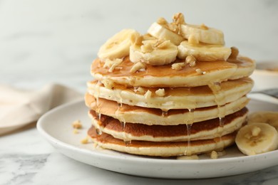 Photo of Delicious pancakes with bananas, walnuts and honey on white marble table, closeup