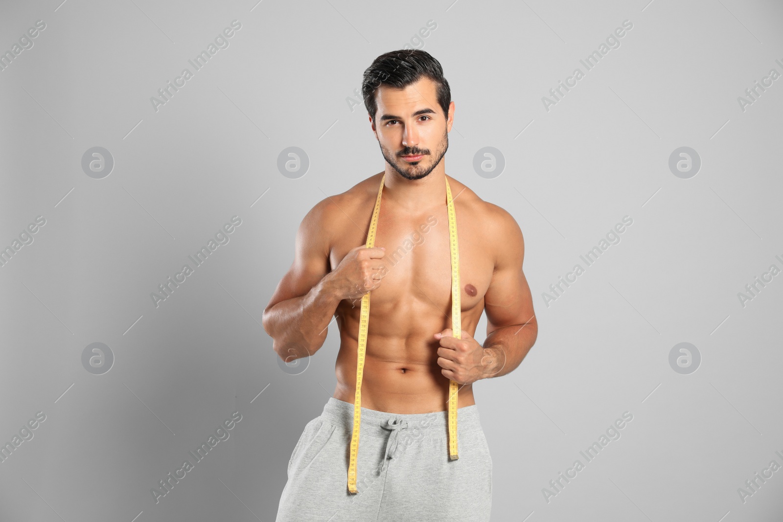 Photo of Young man with slim body using measuring tape on grey background