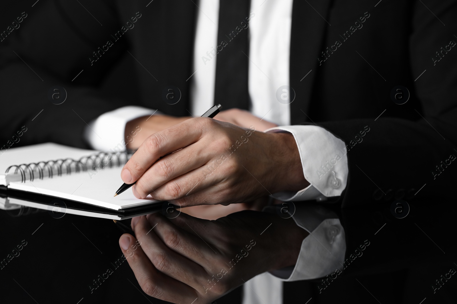 Photo of Man writing in notebook at black table, closeup