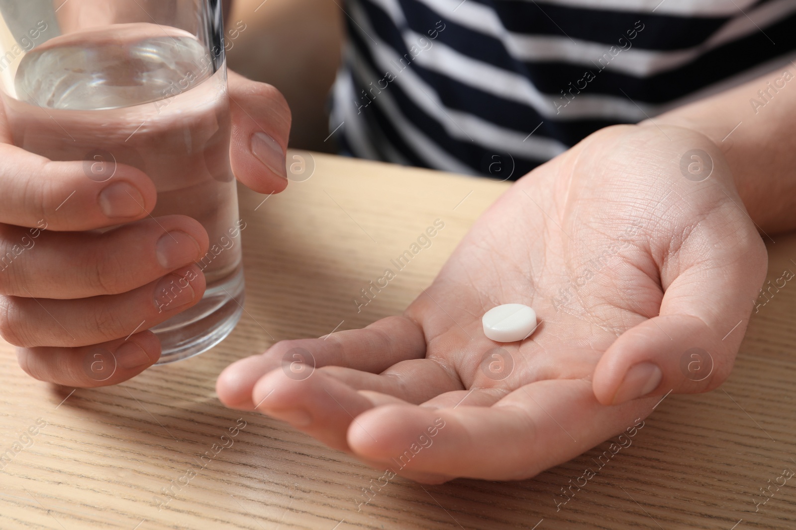 Photo of Man with glass of water and pill at wooden table, closeup