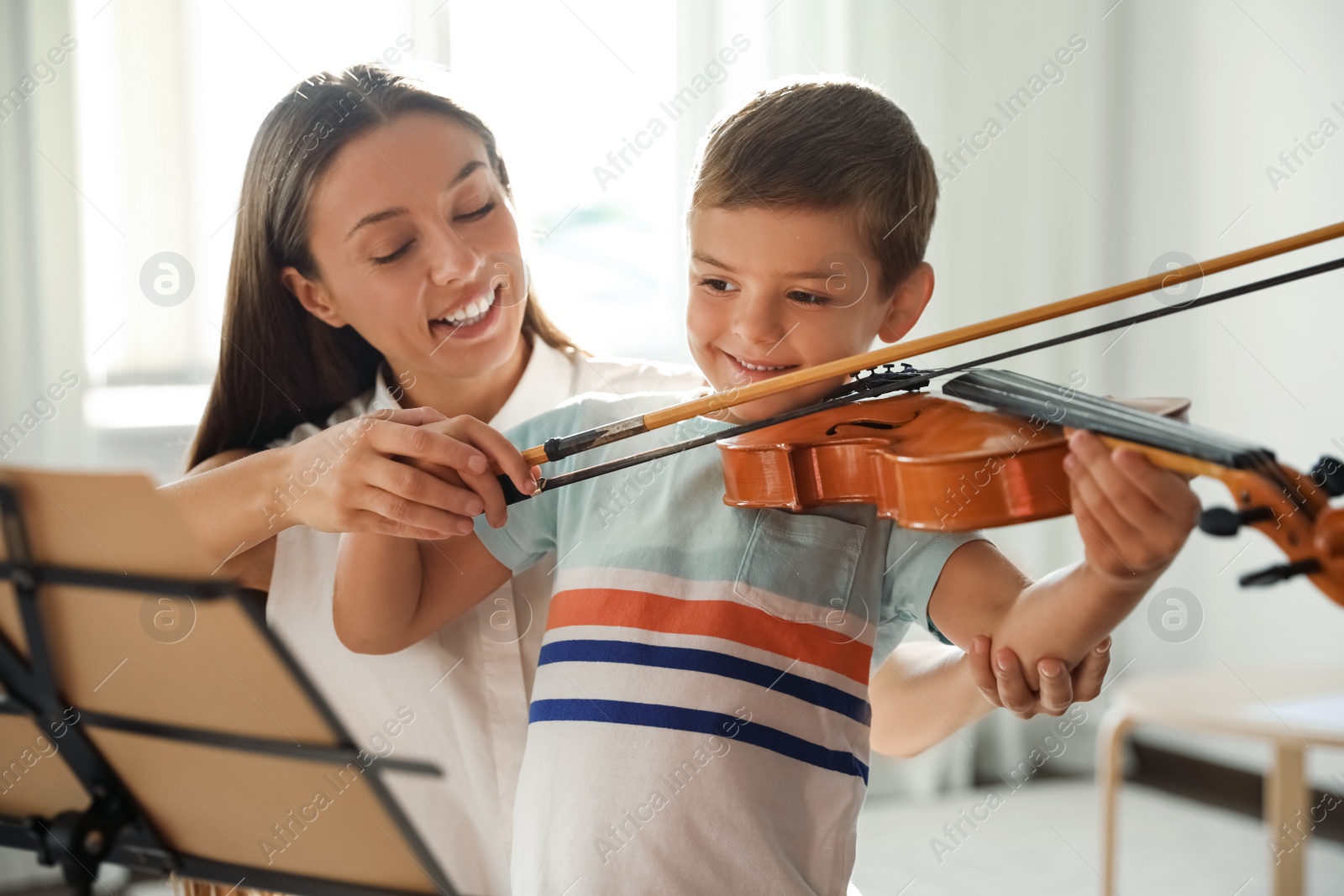 Photo of Young woman teaching little boy to play violin indoors