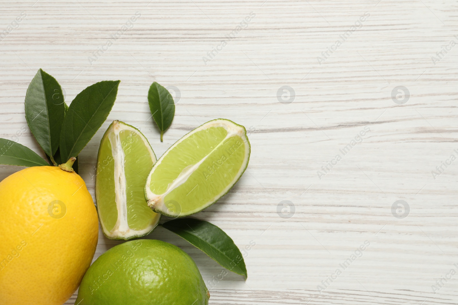 Photo of Fresh ripe lemon, limes and green leaves on white wooden background, flat lay. Space for text