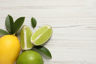 Fresh ripe lemon, limes and green leaves on white wooden background, flat lay. Space for text