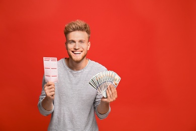 Photo of Portrait of happy young man with money fan and lottery ticket on red background