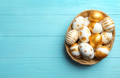 Photo of Wicker basket of traditional Easter eggs decorated with golden paint on wooden background, top view. Space for text