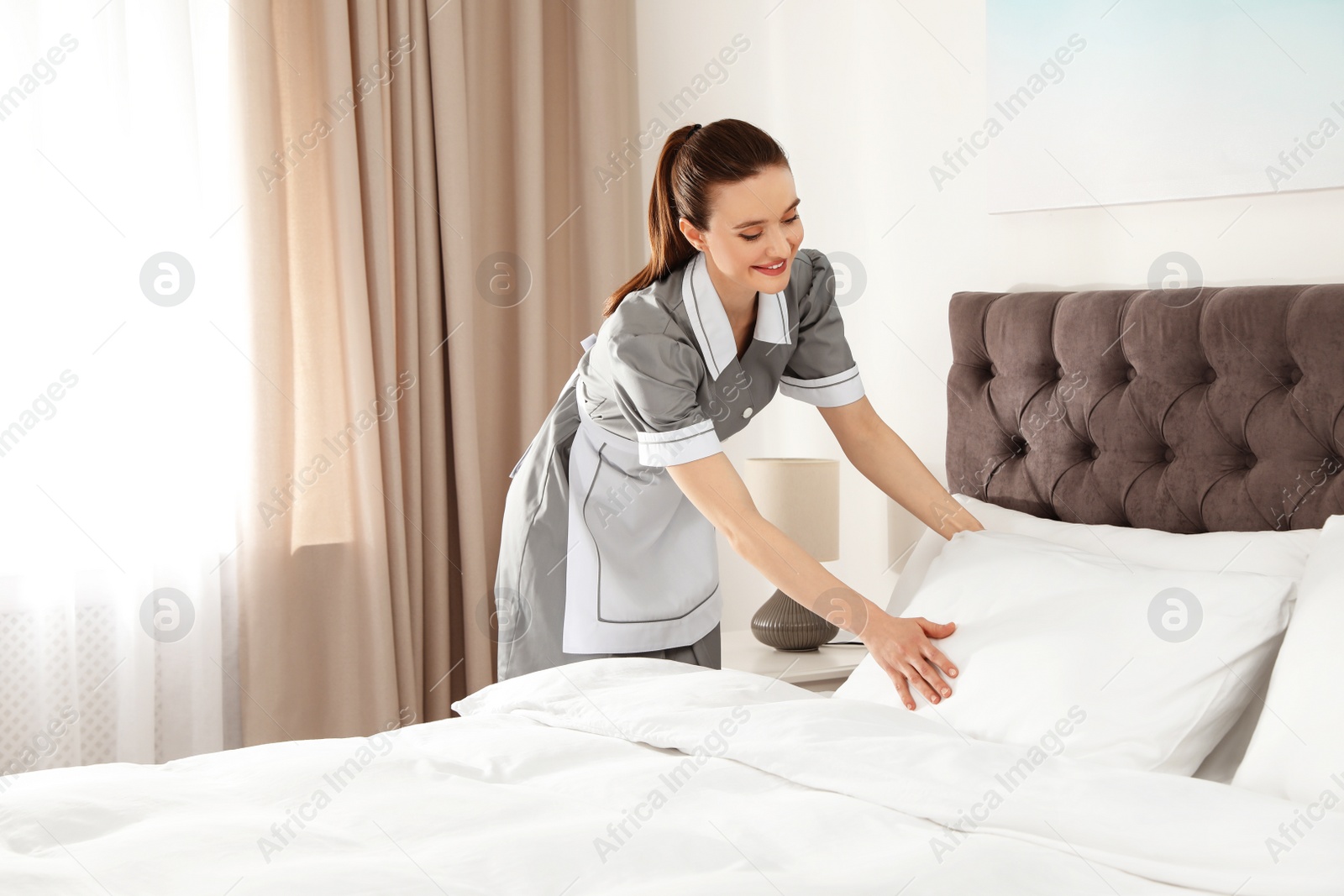 Photo of Young chambermaid making bed in hotel room