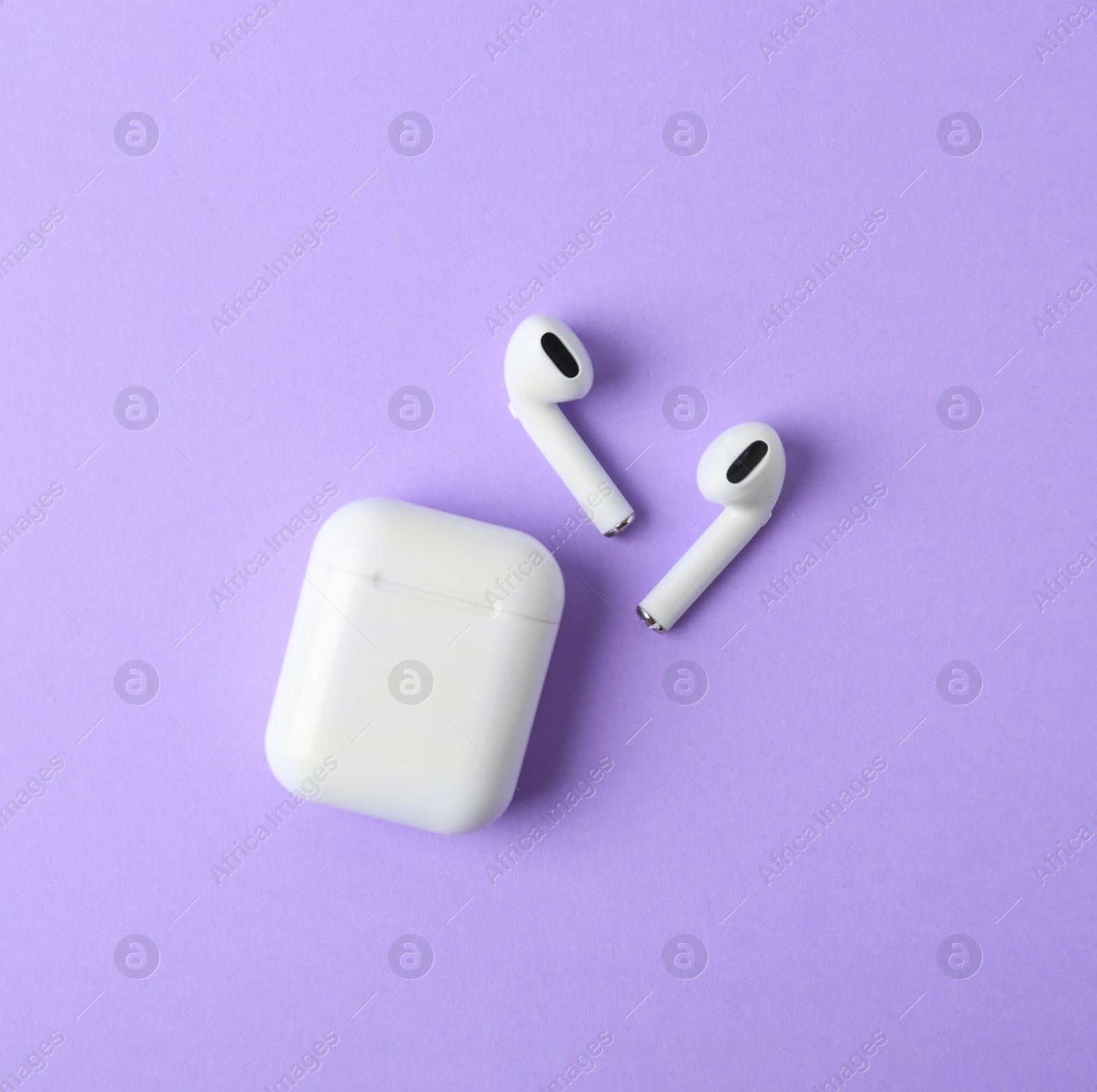 Photo of Modern wireless earphones and charging case on violet background, flat lay