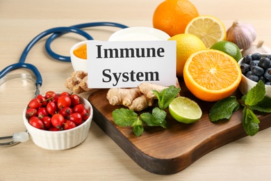 Photo of Card with phrase Immune System, stethoscope and fresh products on wooden table. Closeup