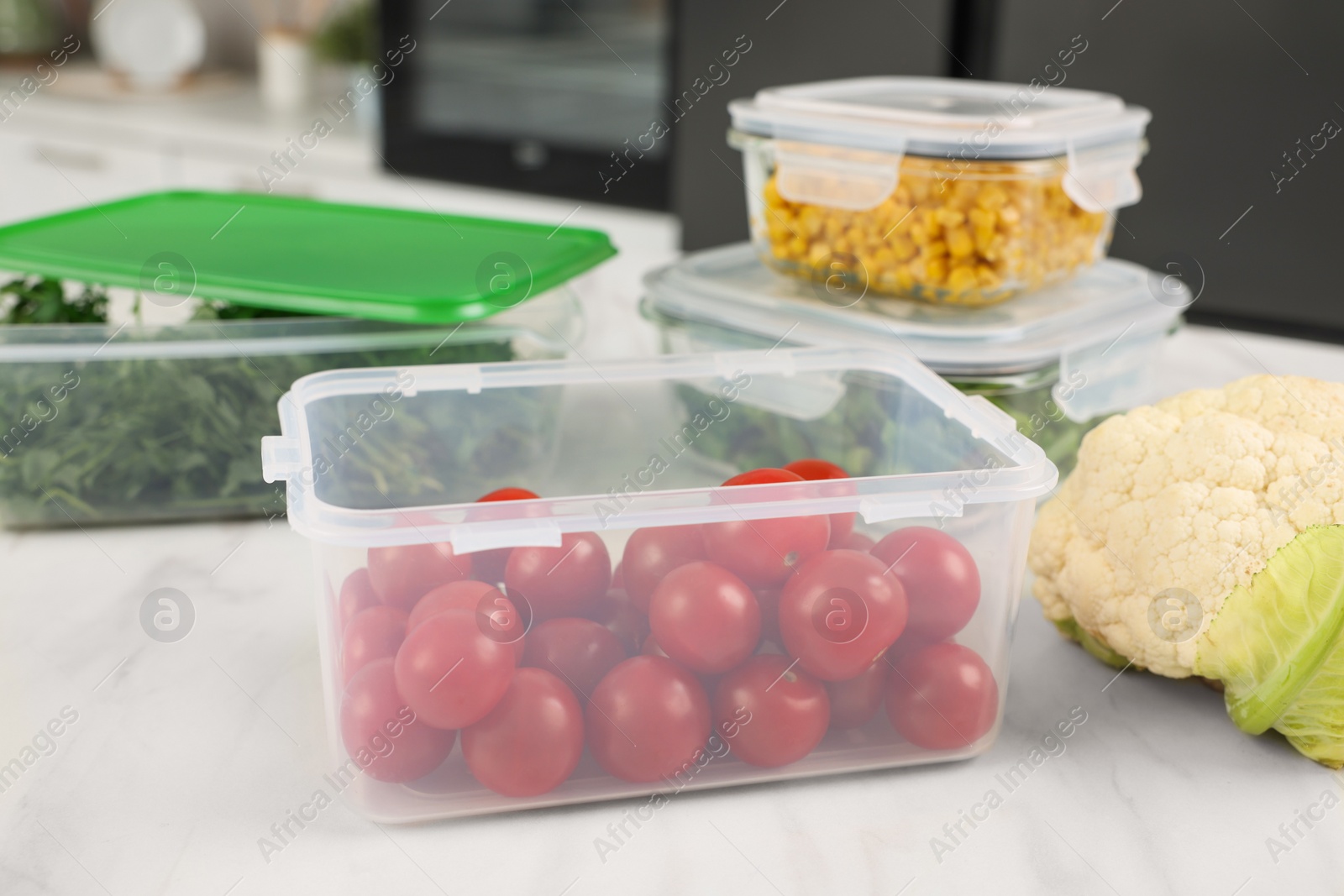 Photo of Containers with cherry tomatoes and fresh products on white marble table in kitchen. Food storage