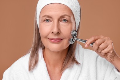 Photo of Woman massaging her face with metal roller on brown background, closeup