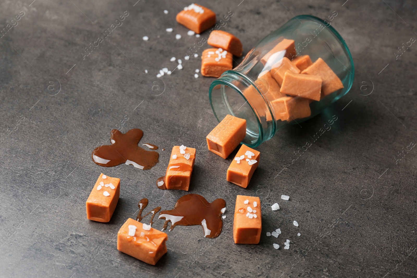 Photo of Delicious caramel candies with sauce and salt on gray background