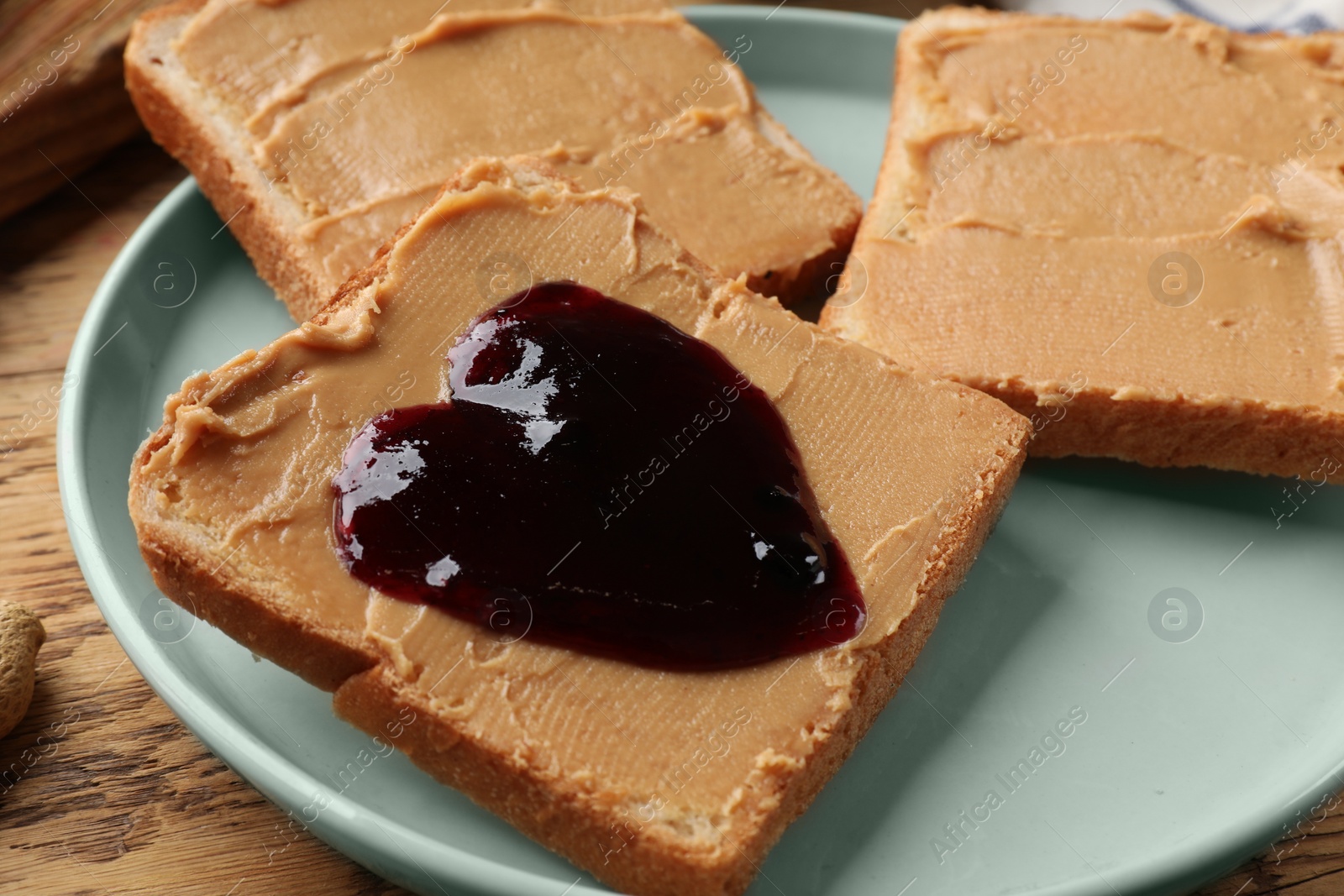 Photo of Tasty peanut butter sandwiches with jam on wooden table, closeup