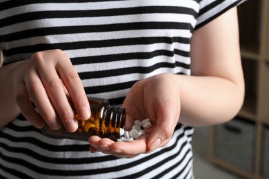 Woman pouring pills from bottle on blurred background, closeup