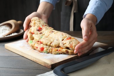 Photo of Woman making Stollen with candied fruits and raisins on wooden board at table, closeup