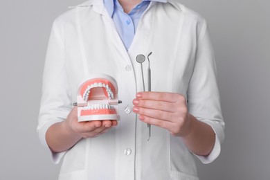 Photo of Dentist holding jaws model and tools on light grey background, closeup