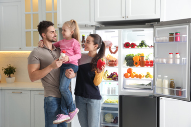 Photo of happy family with products near open refrigerator in kitchen