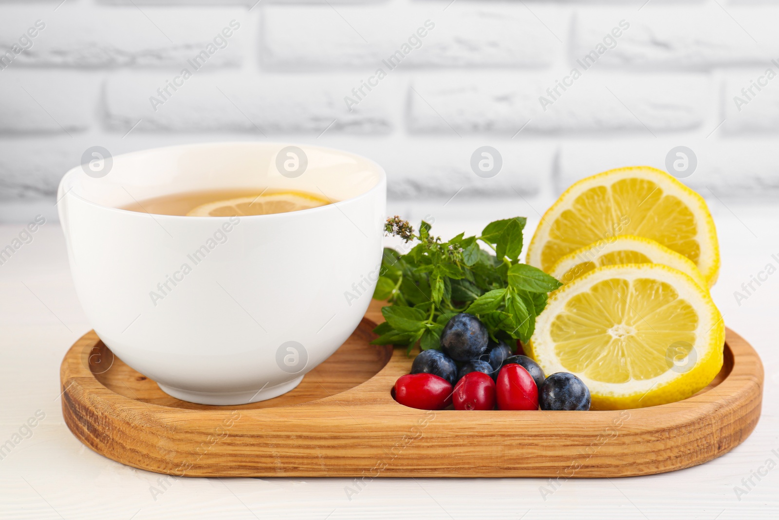 Photo of Cup with delicious immunity boosting tea and ingredients on white wooden table, closeup