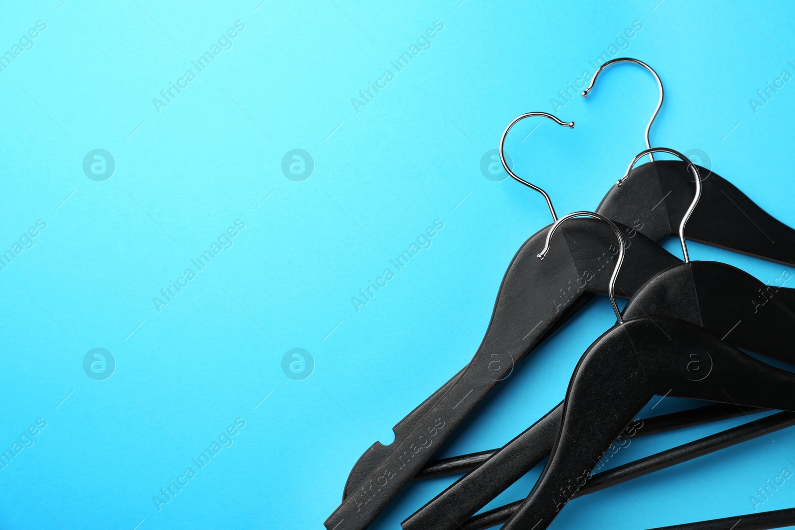 Photo of Black hangers on light blue background, top view. Space for text