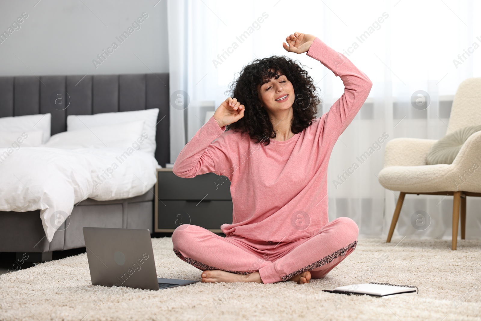 Photo of Beautiful young woman in stylish pyjama with laptop and notebook on floor at home