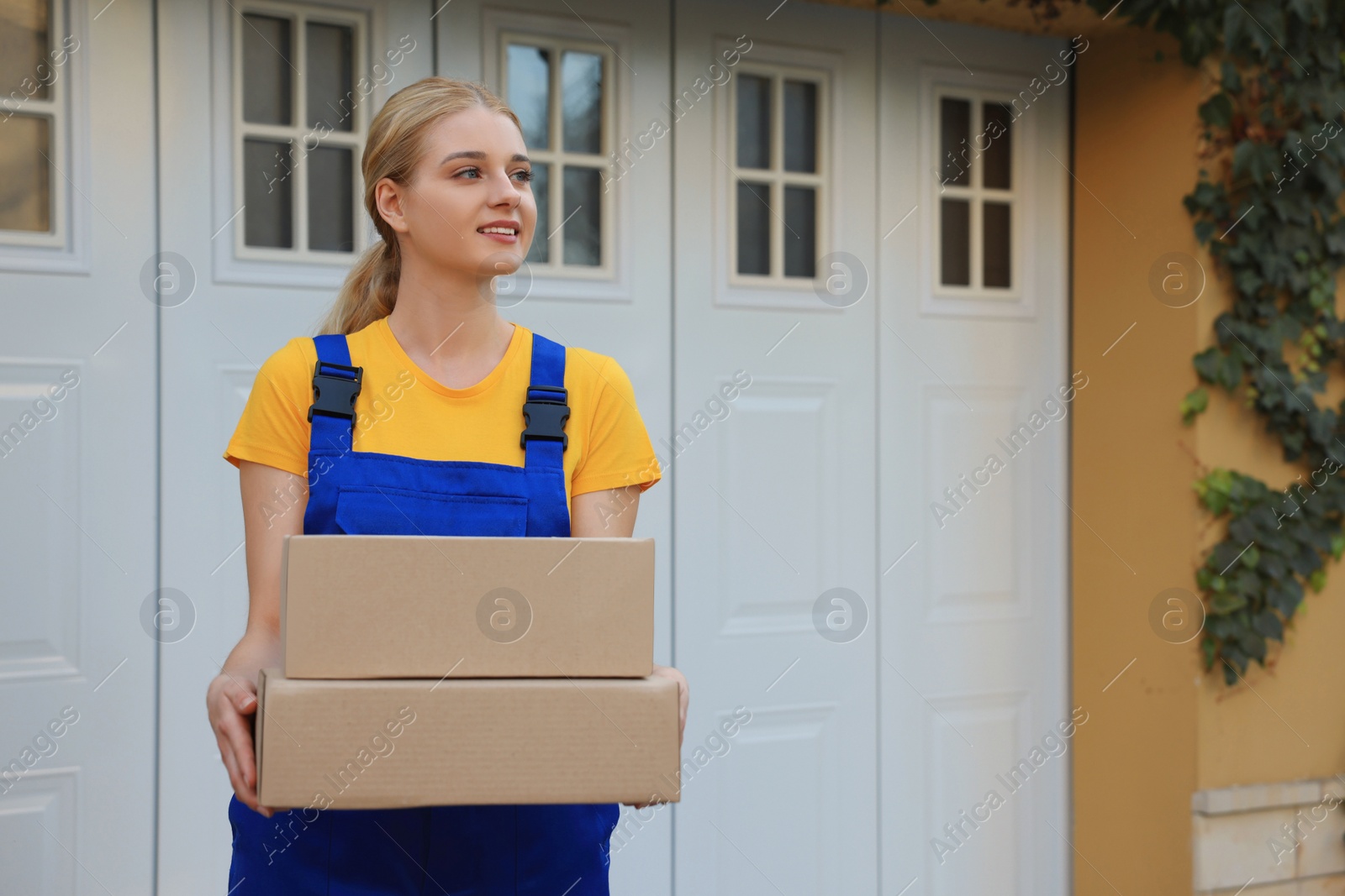 Photo of Courier in uniform with parcels near private house outdoors, space for text