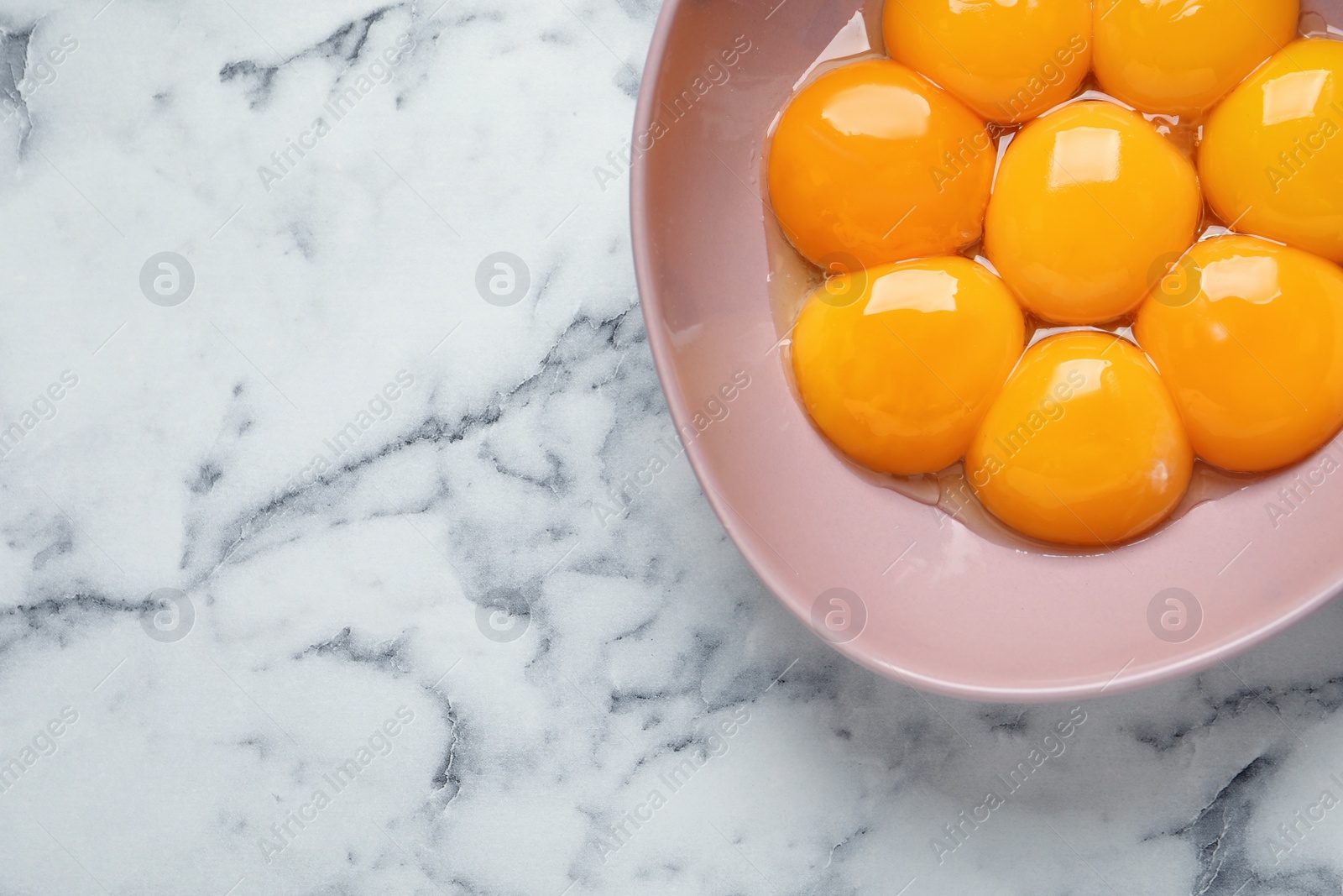 Photo of Bowl with raw egg yolks on white marble table, top view. Space for text