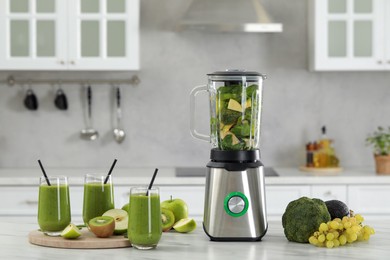 Photo of Delicious fresh smoothie and blender with ingredients on white marble table in kitchen