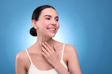 Beautiful woman with smear of body cream on her neck against light blue background. Space for text