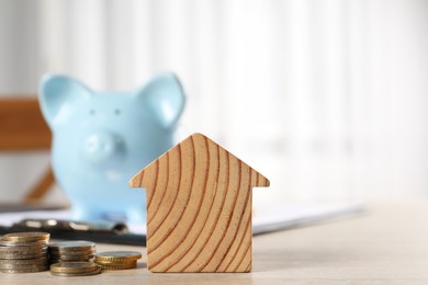 Photo of House model, piggy bank, clipboard and coins on wooden table indoors, selective focus. Space for text