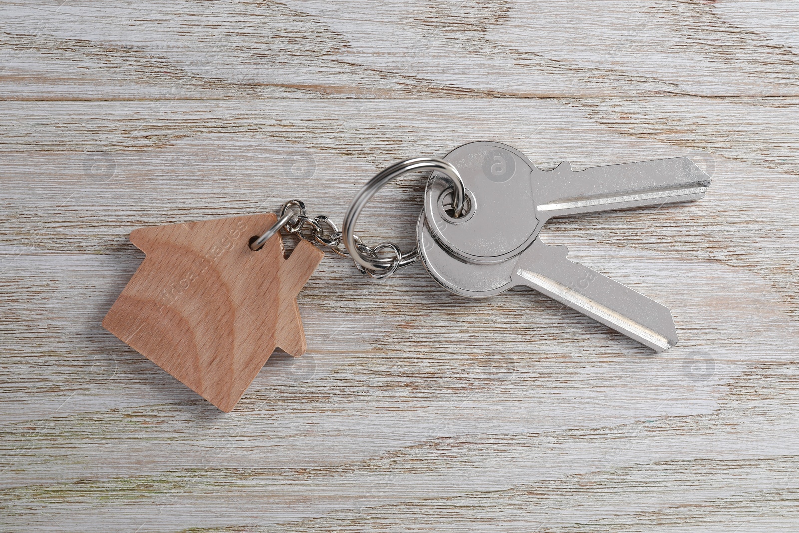 Photo of Keys with keychain in shape of house on light wooden table, top view