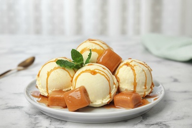Photo of Delicious ice cream served with caramel and sauce on marble table