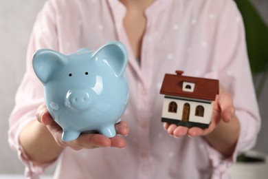 Woman with house model and piggy bank indoors, selective focus