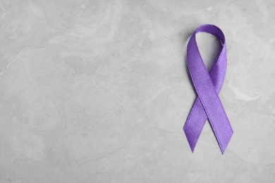 Purple ribbon on grey stone background, top view with space for text. Domestic violence awareness