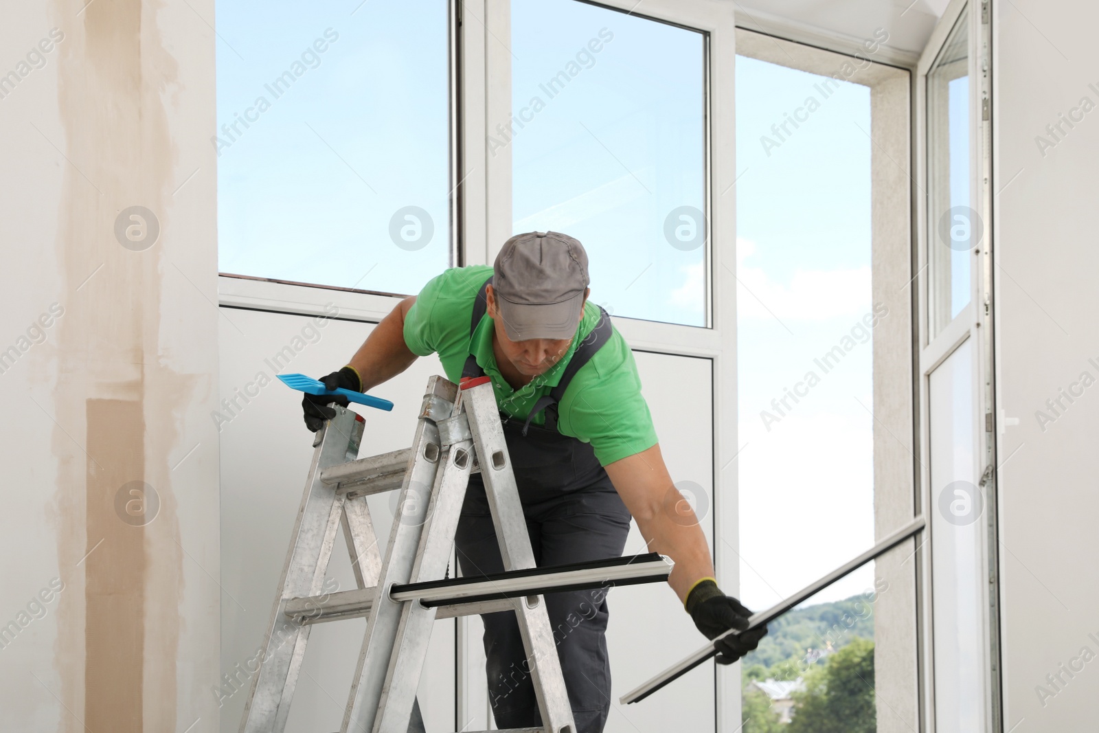 Photo of Worker on folding ladder installing window indoors