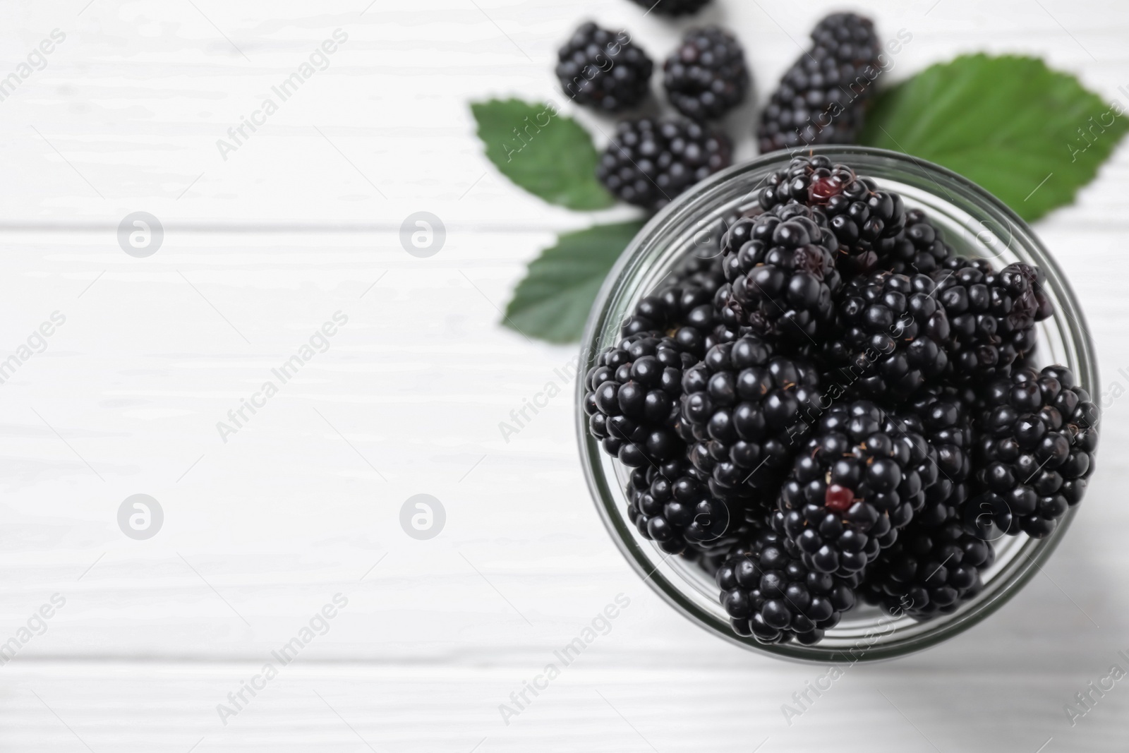 Photo of Fresh ripe blackberries in glass jar on white wooden table, closeup. Space for text