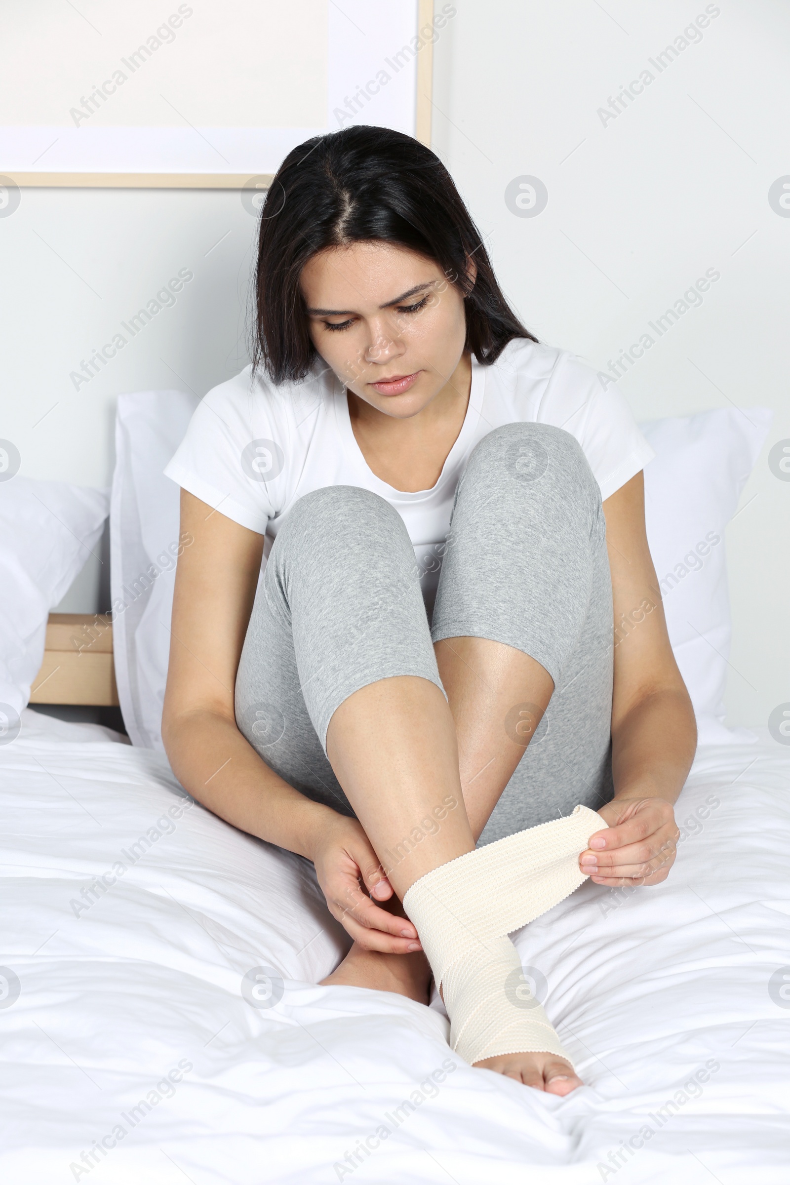 Photo of Young woman applying medical bandage onto foot in bedroom