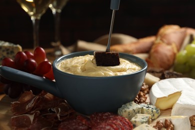 Dipping piece of bread into fondue pot with melted cheese at table, closeup