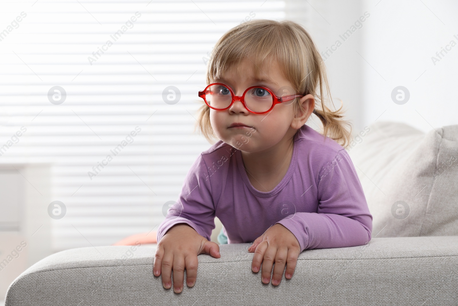 Photo of Cute little girl in glasses on sofa at home. Space for text