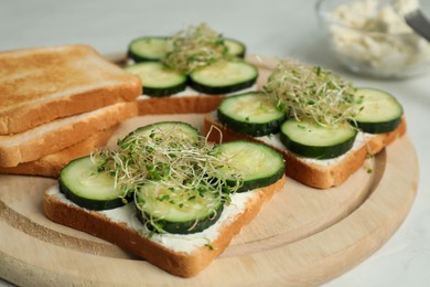 Photo of Tasty toasts with cucumber, cream cheese and microgreens on white table, closeup