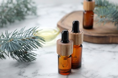Photo of Bottles of spruce essential oil and fresh twigs on white marble table