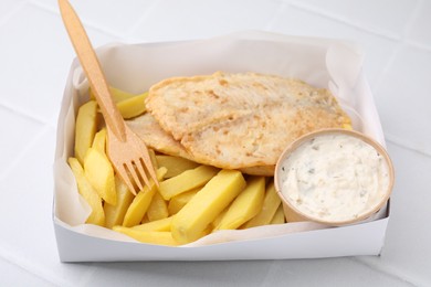 Delicious fish and chips with tasty sauce served on white tiled table, closeup