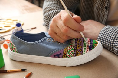 Photo of Man painting on sneaker at table, closeup. Customized shoes